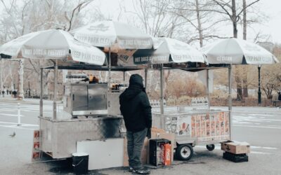 Food cart with umbrellas in a park setting, vendor standing nearby, showcasing outdoor dining options.
